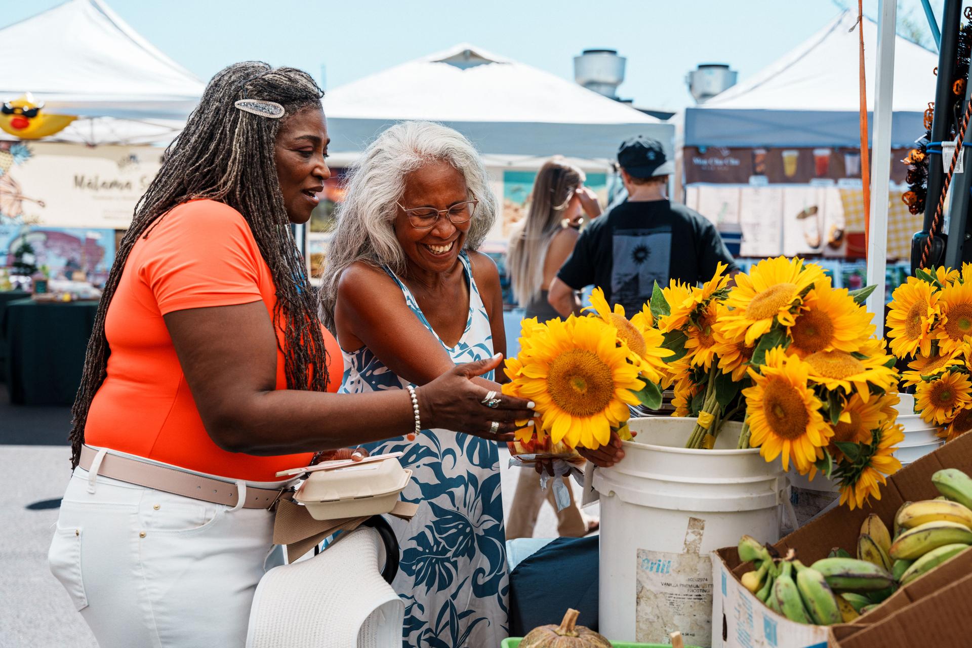 Hawaiian local tour guide and senior client looking at flowers together at the farmer's market